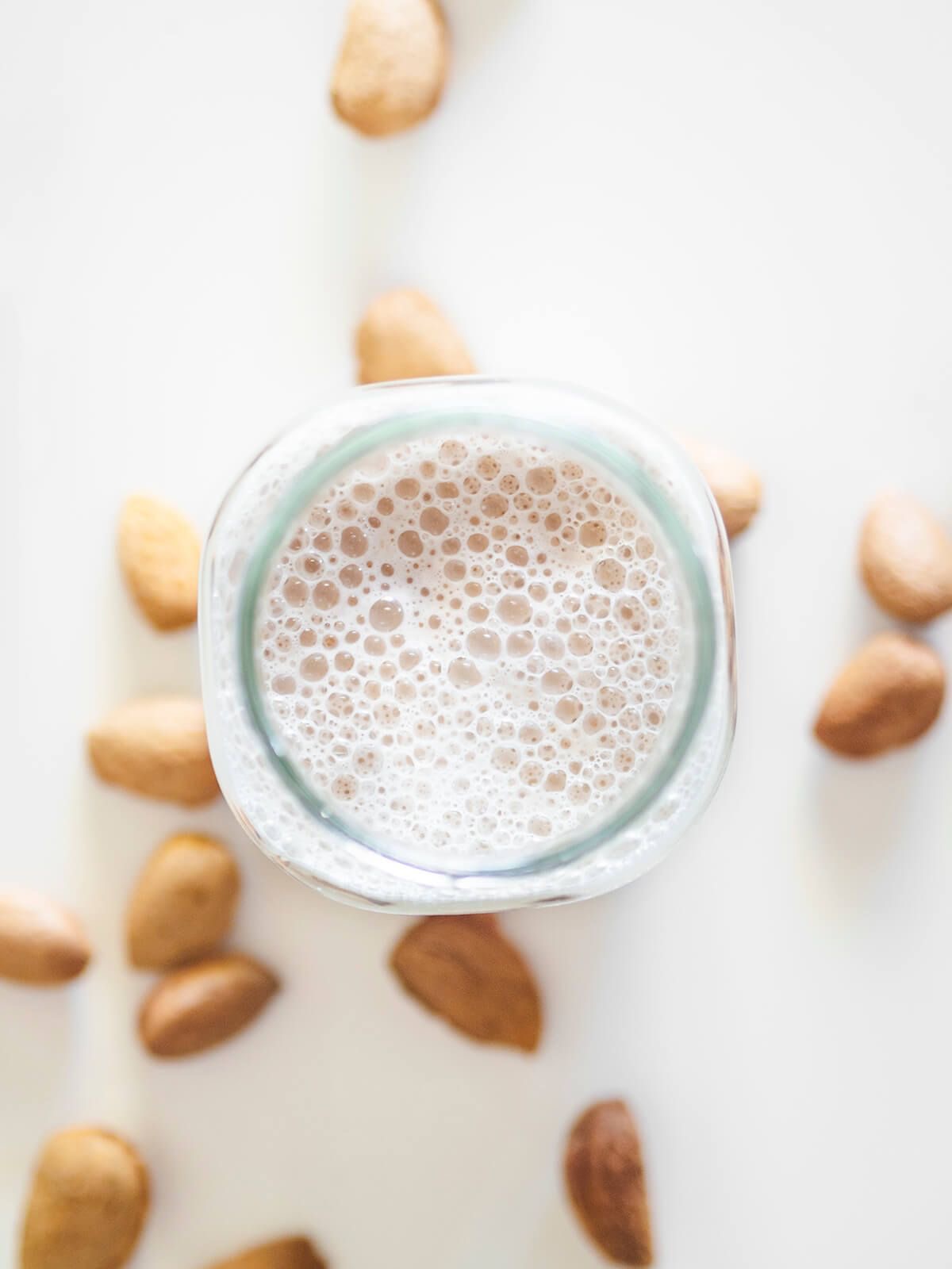 Vaso de vidrio con leche de almendra siendo servida y un bowl de almendras al lado